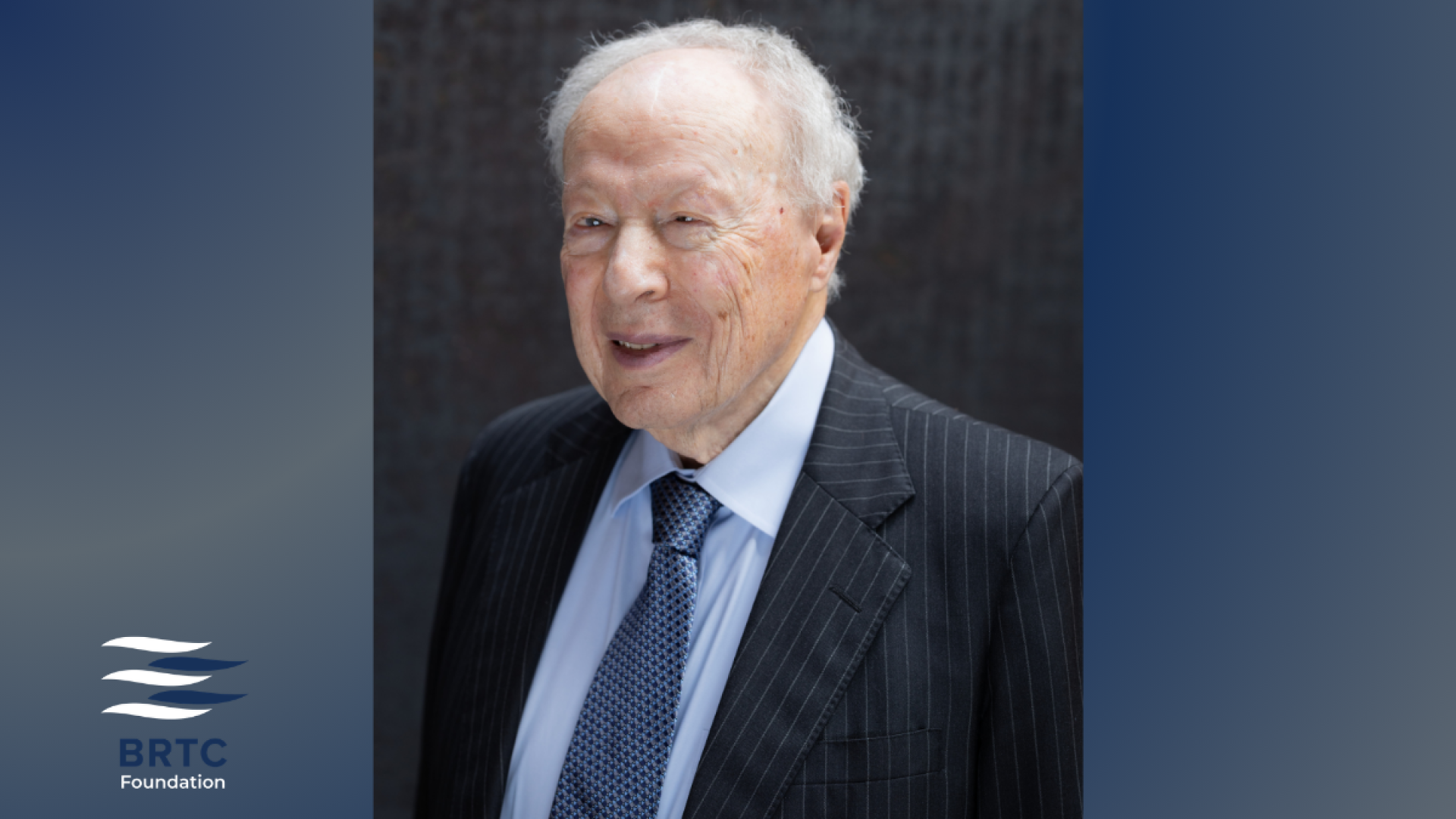 An elderly man with white hair, wearing a pinstriped suit and patterned tie, smiles in a portrait against a dark textured background, with the BRTC Foundation logo.